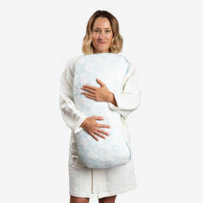 Image of a woman in a Dr. Weil Featherweight Robe standing up and hugging the Cooling Crescent Shredded Foam Pillow against her