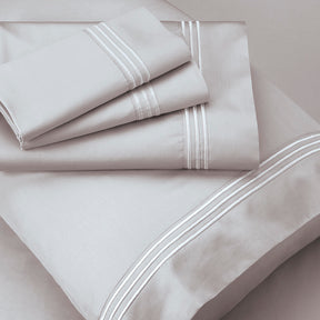 Image of Dove Gray Recovery Cotton Shed Set shown top to bottom with two folded pillowcases, one flat sheet, a pillowcase shown on a pillow, and a fitted sheet underneath