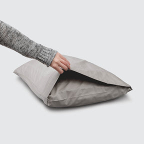 Image of a Dove Gray Bamboo Rayon Pillowcase on a pillow with a hand lifting up the edge to showcase the enveloping design