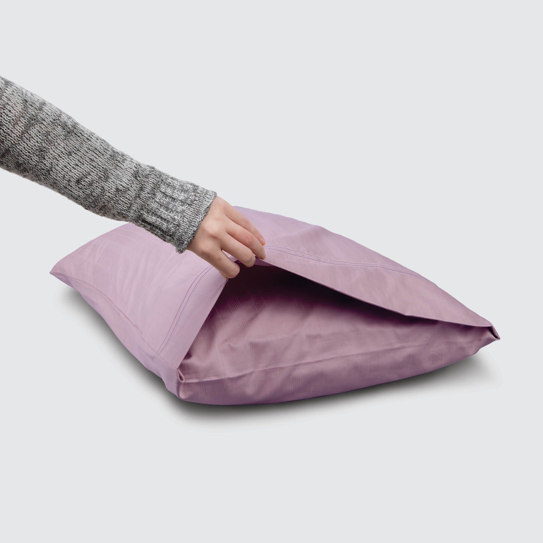 Image of a Lilac Bamboo Rayon Pillowcase on a pillow with a hand lifting up the edge to showcase the enveloping design