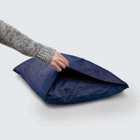 Image of a Midnight Bamboo Rayon Pillowcase on a pillow with a hand lifting up the edge to showcase the enveloping design