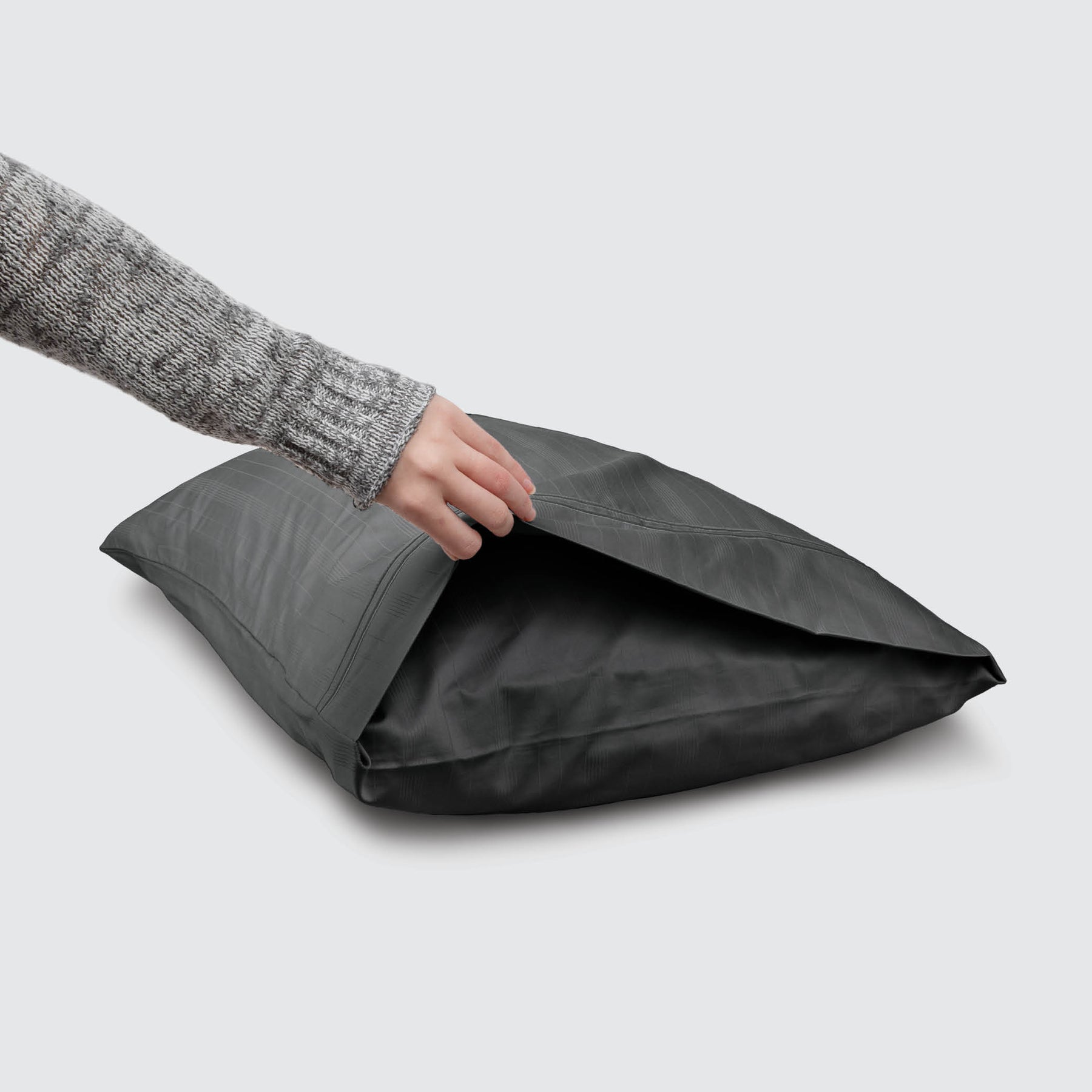 Image of a Shadow Bamboo Rayon Pillowcase on a pillow with a hand lifting up the edge to showcase the enveloping design