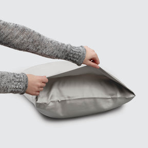 Image of a Dove Gray Soft Touch TENCEL™ Modal Pillowcase on a pillow with a hand lifting up the edge to showcase the enveloping design