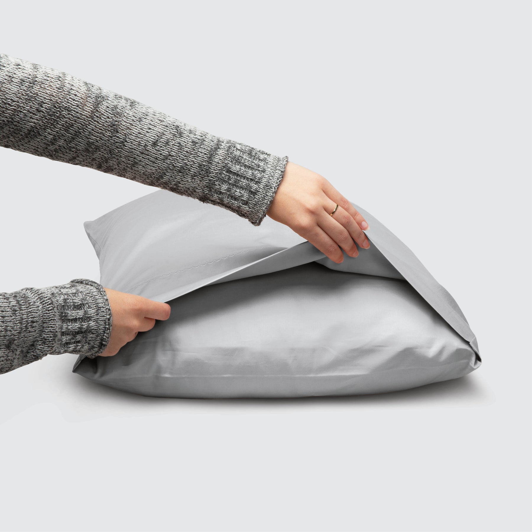 Image of a Coastal Gray Weightless Cotton Pillowcase on a pillow with a hand lifting up the edge to showcase the enveloping design