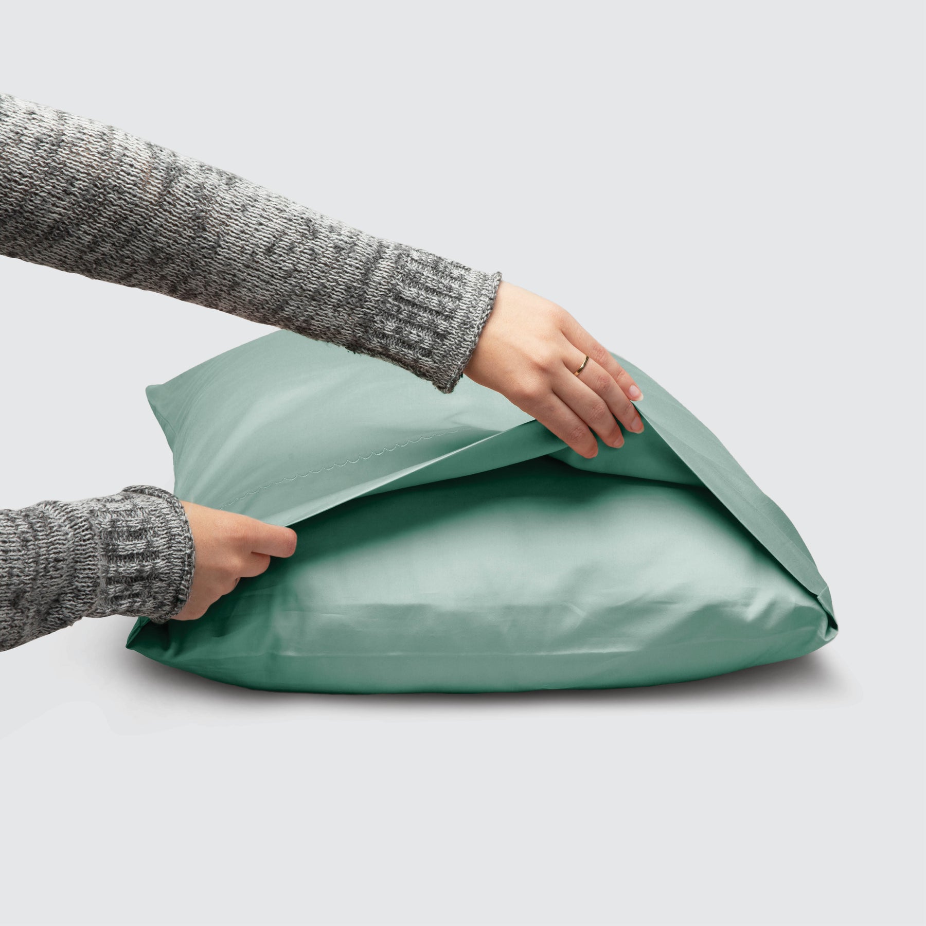 Image of a Seafoam Weightless Cotton Pillowcase on a pillow with a hand lifting up the edge to showcase the enveloping design