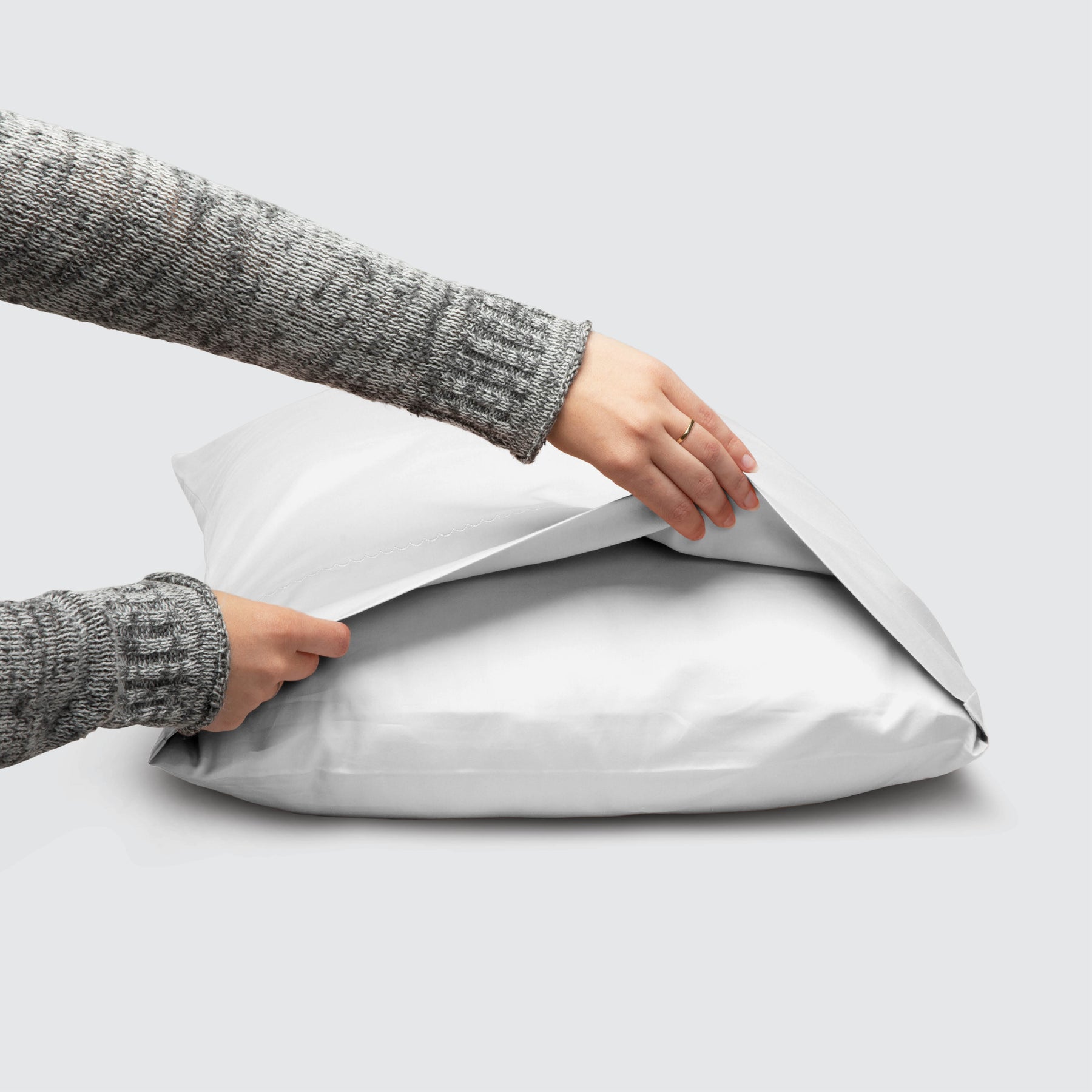 Image of a White Weightless Cotton Pillowcase on a pillow with a hand lifting up the edge to showcase the enveloping design