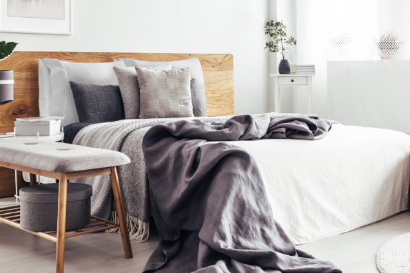 Image of a white bed in a light, neutral-colored room with various gray accent pillows and blankets on the bed